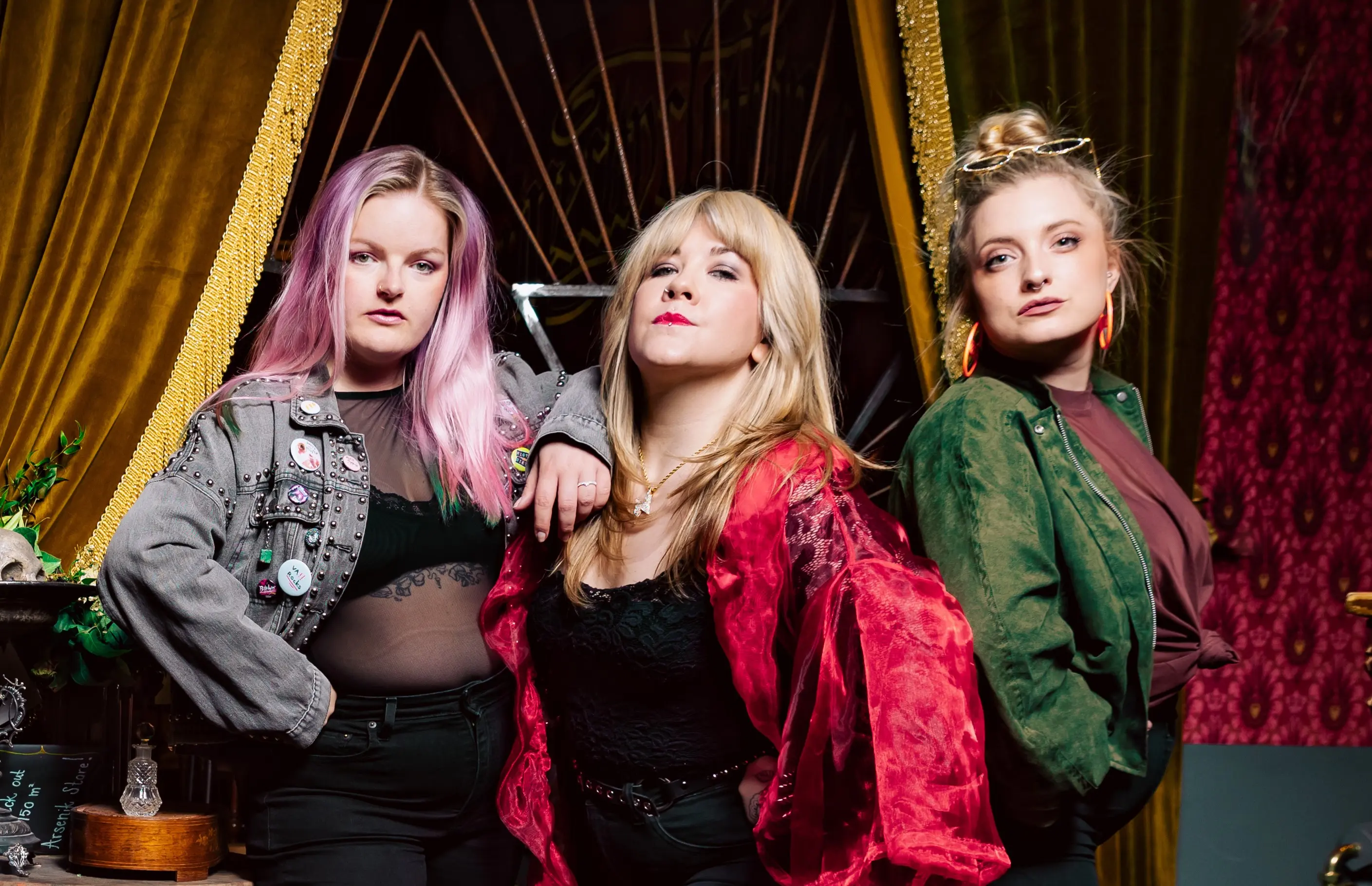 Ett rockband bestående av tre färgglada kvinnor står uppställda och tittar allvarligt in i kameran.