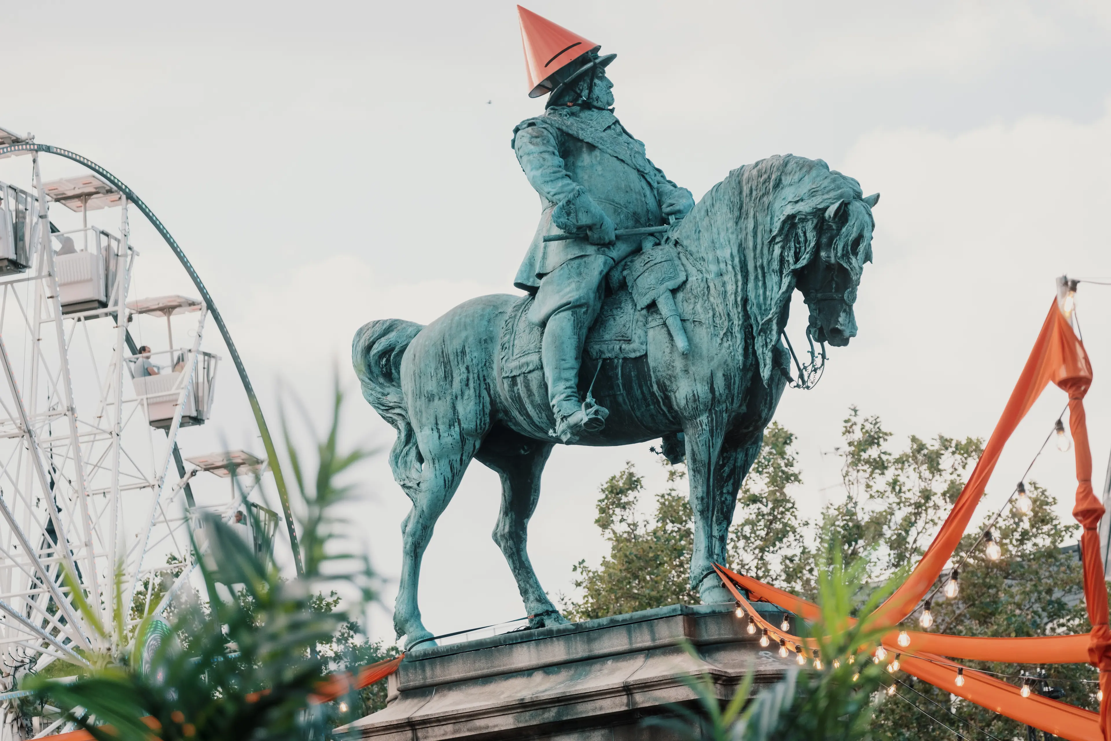 Ryttarstaty med orange hatt och festivaldekorationer i stadsmiljö.